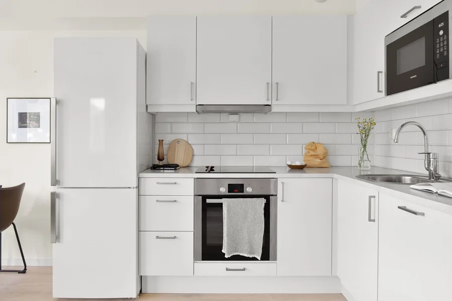 Helle weiße Küchenzeile mit Fliesenspiegel und Einbaugeräten als Beispiel für eine Studio-Planung