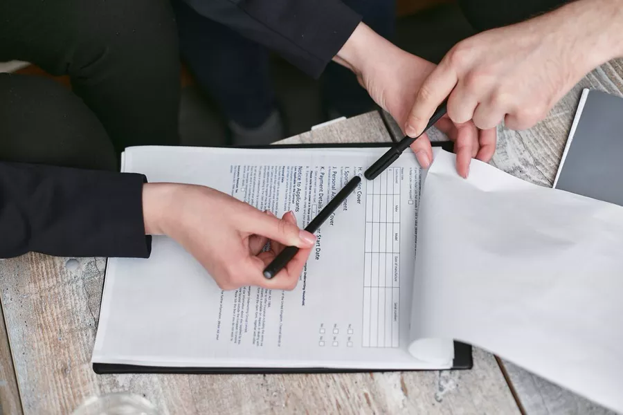 Nahaufnahme von Händen, die einen Vertrag mit Stift auf Unterlagen prüfen